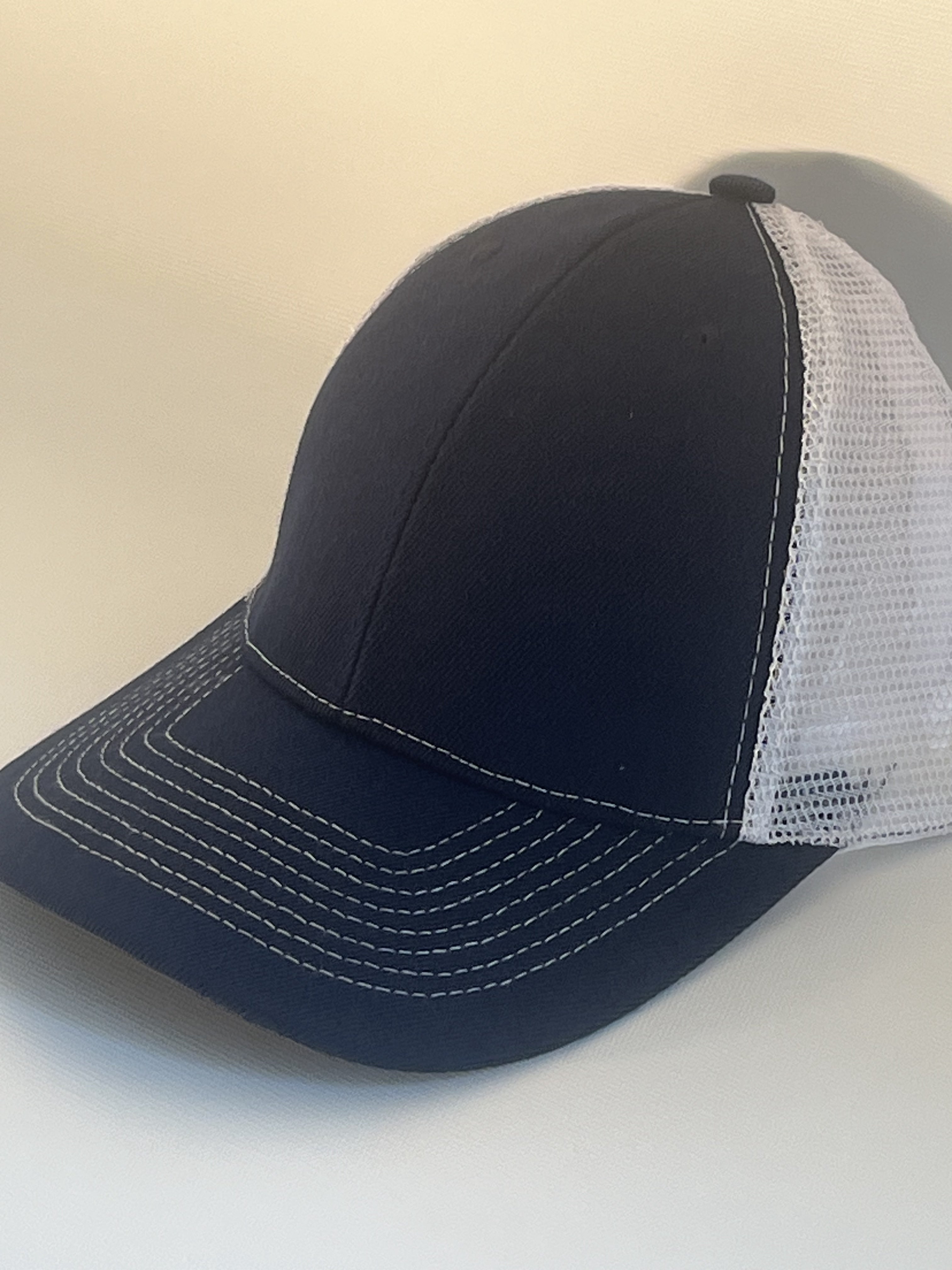 A dark navy blue trucker-style baseball cap with white contrast stitching on the brim and a white mesh back.
