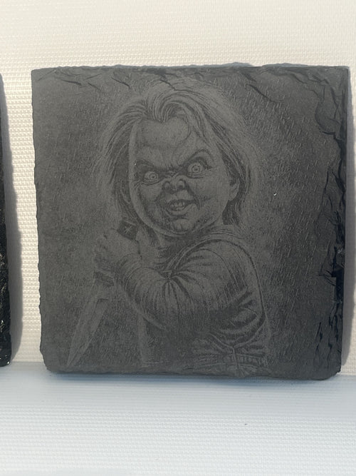 A square dark gray slate coaster featuring an embossed portrait of Chucky.