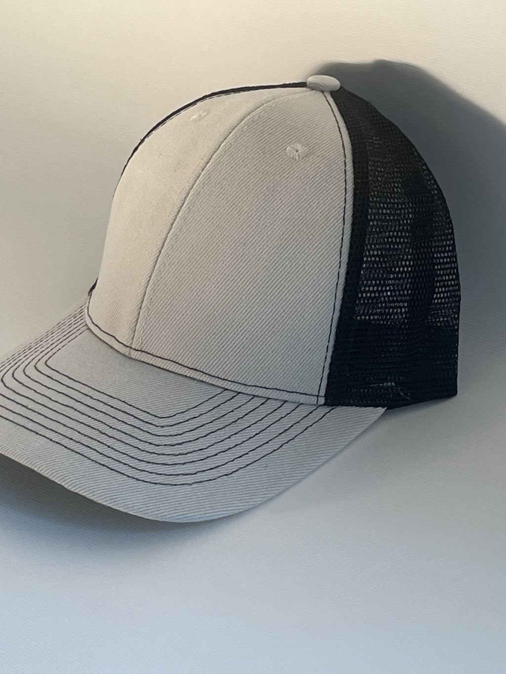 A two-tone trucker cap with a light gray front panel and brim, and a black mesh back.