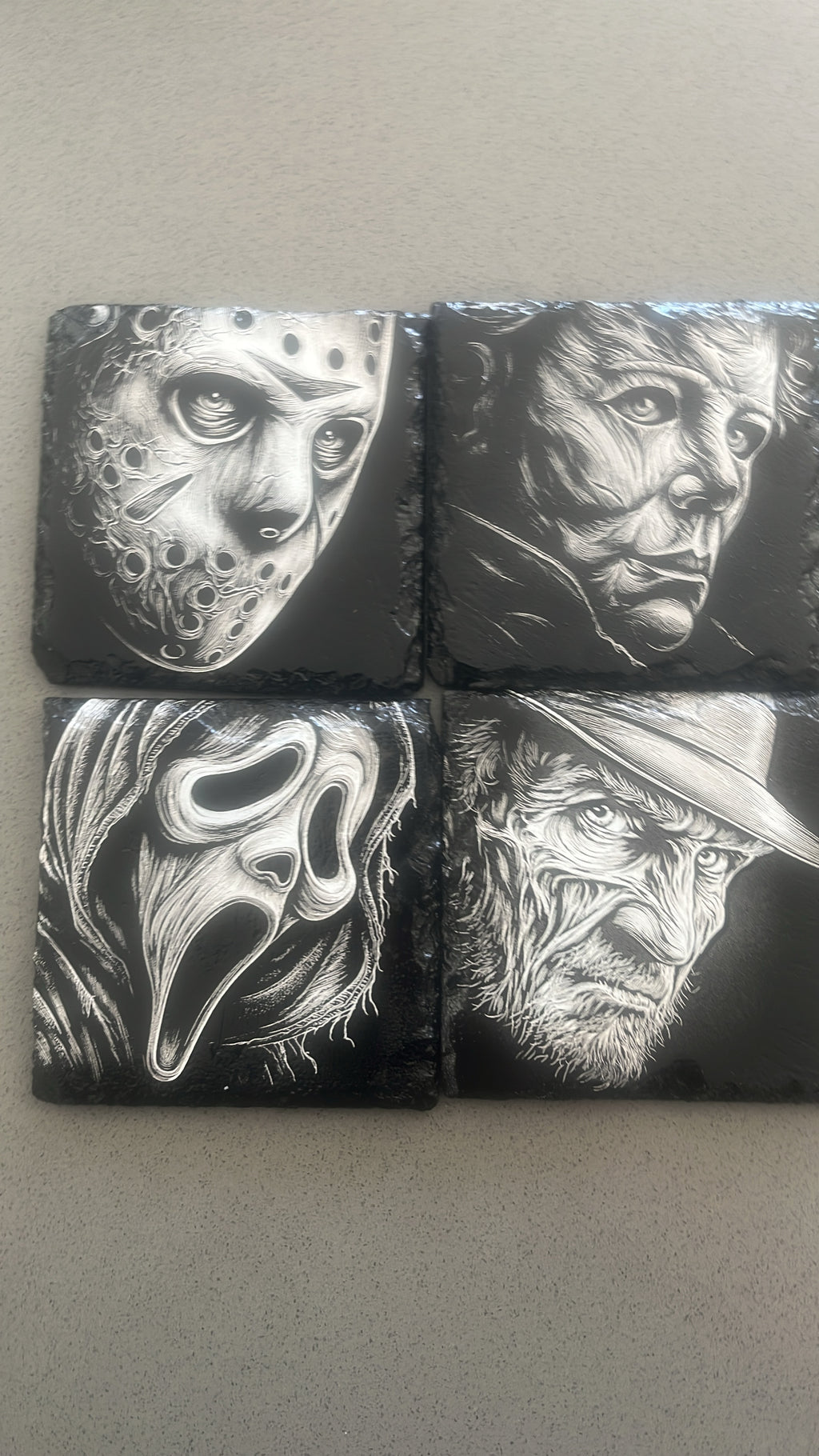 Four square black coasters featuring detailed black and white illustrations of horror movie villains: Jason Voorhees, Michael Myers, Sally the Screaming Mask, and Freddy Krueger.