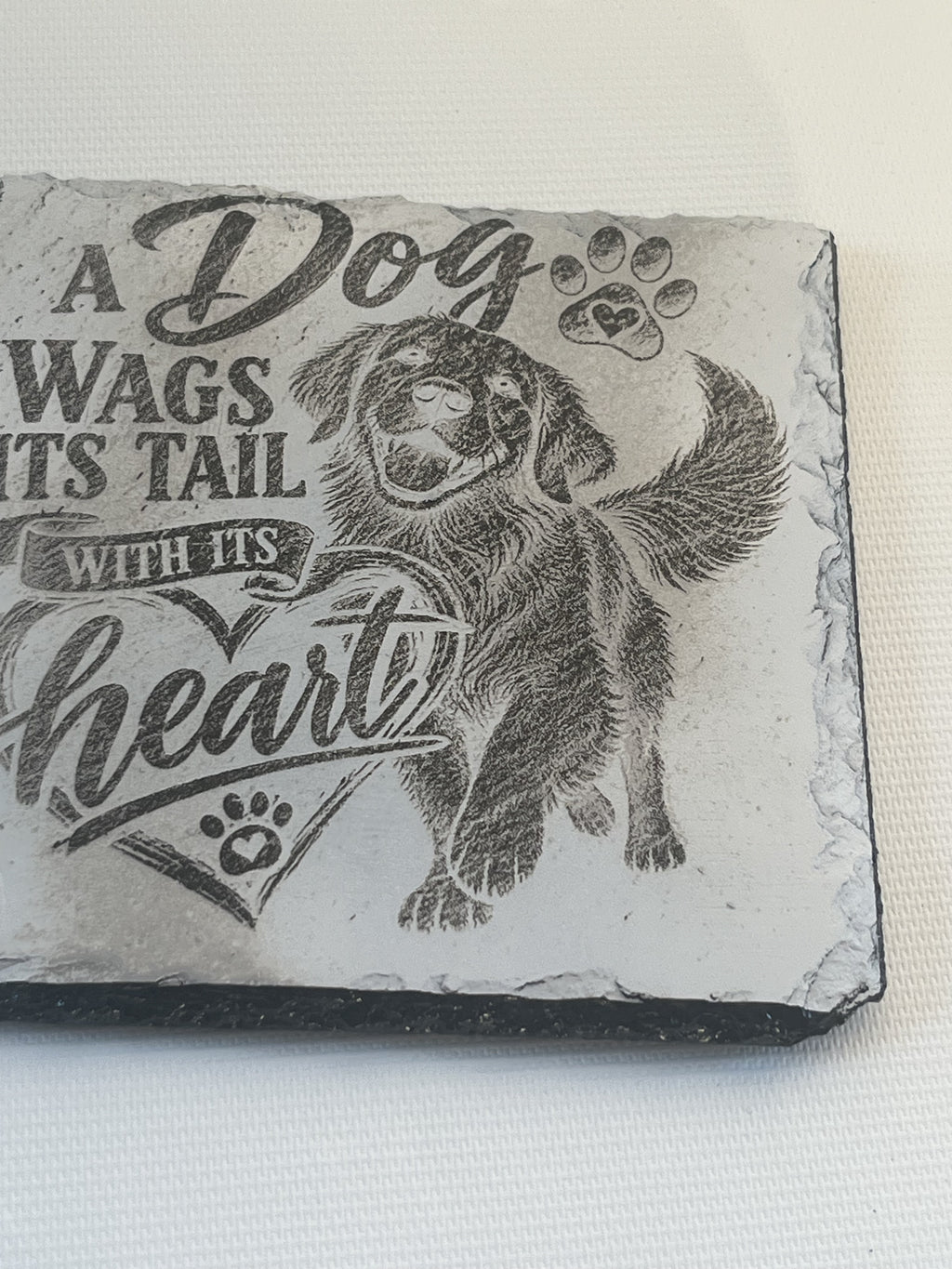A rectangular slate plaque featuring a black engraved illustration of a golden retriever dog and the text 'A Dog Wags Its Tail WITH ITS heart'.