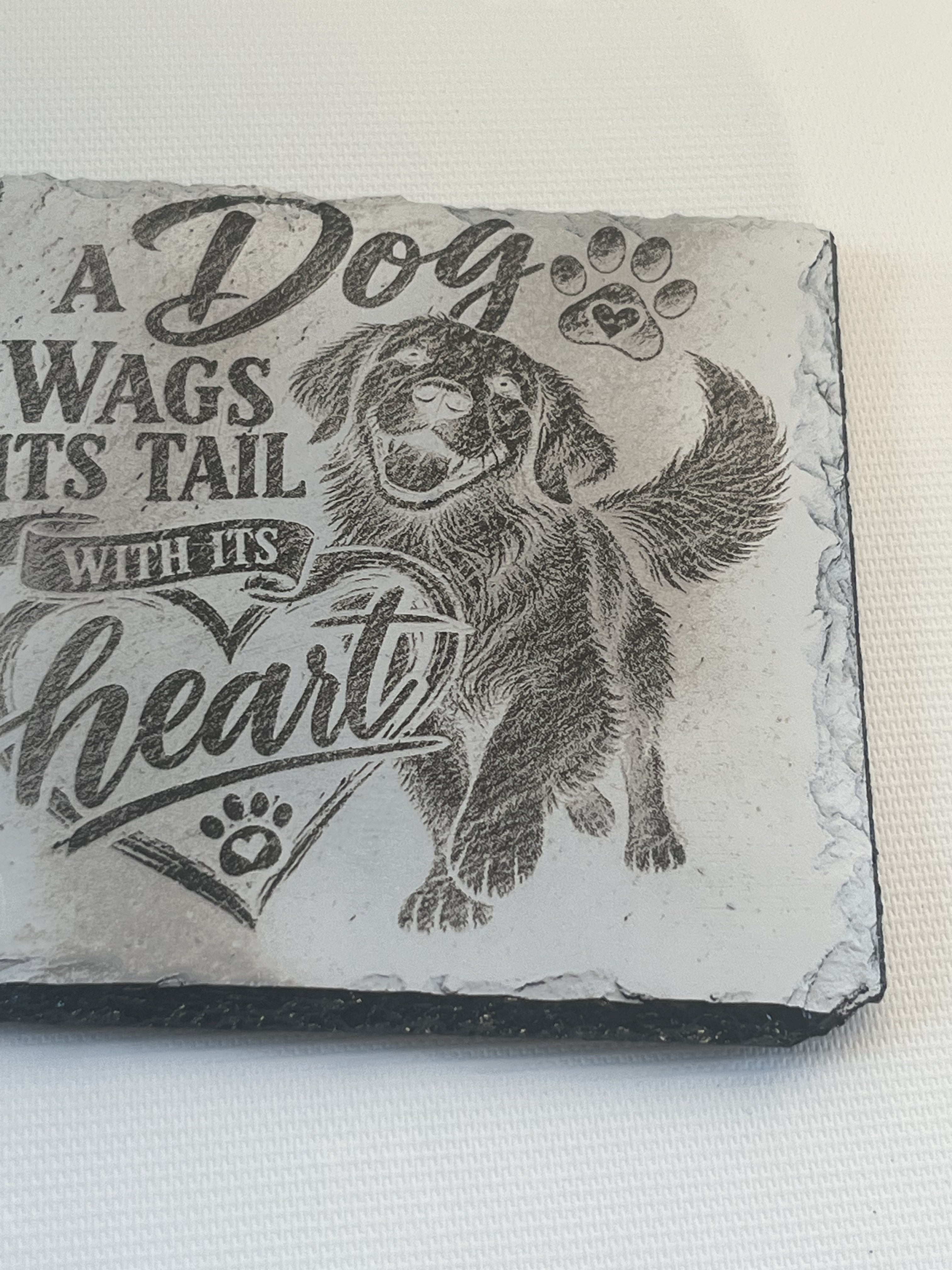A rectangular slate plaque featuring a black engraved illustration of a golden retriever dog and the text 'A Dog Wags Its Tail WITH ITS heart'.
