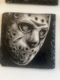 A square black slate coaster featuring a highly detailed black and white graphic illustration of a hockey mask.