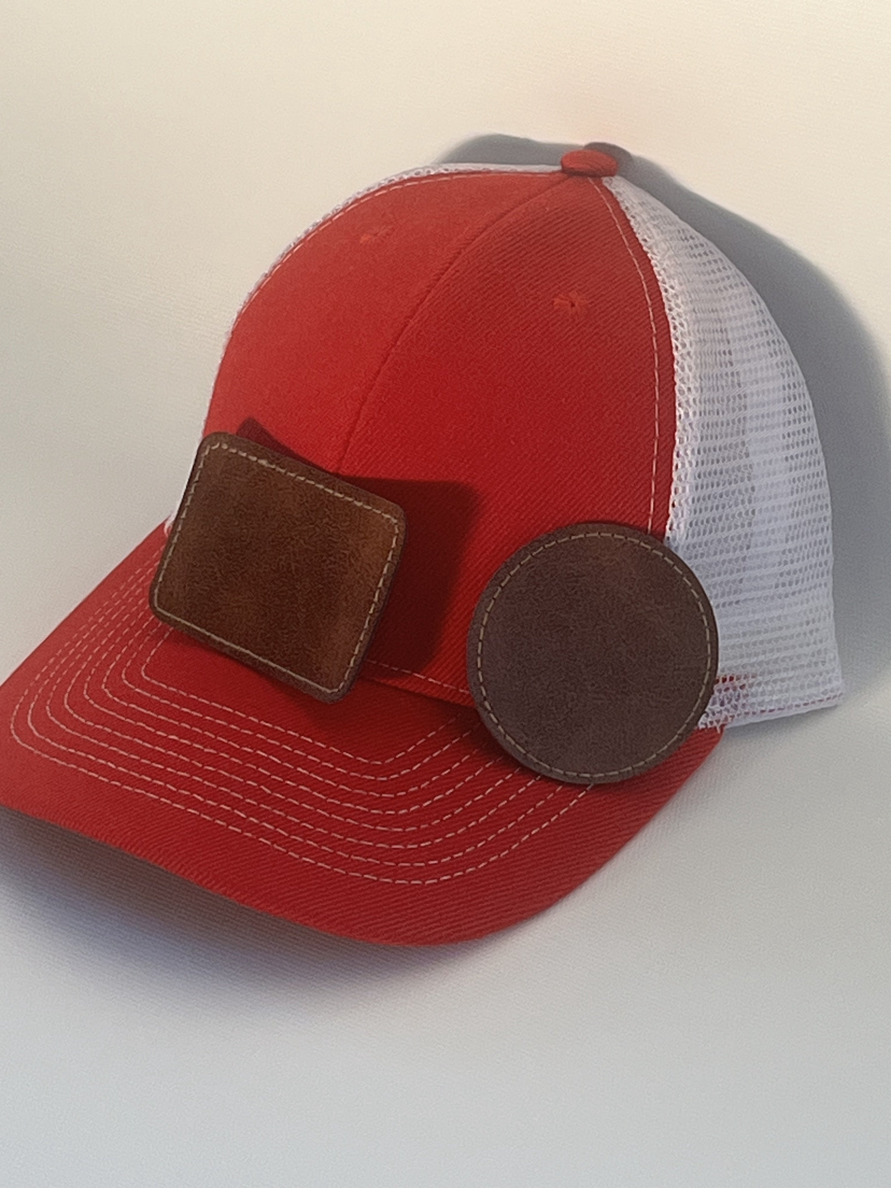 A red and white trucker-style cap with brown leather patches on the front.
